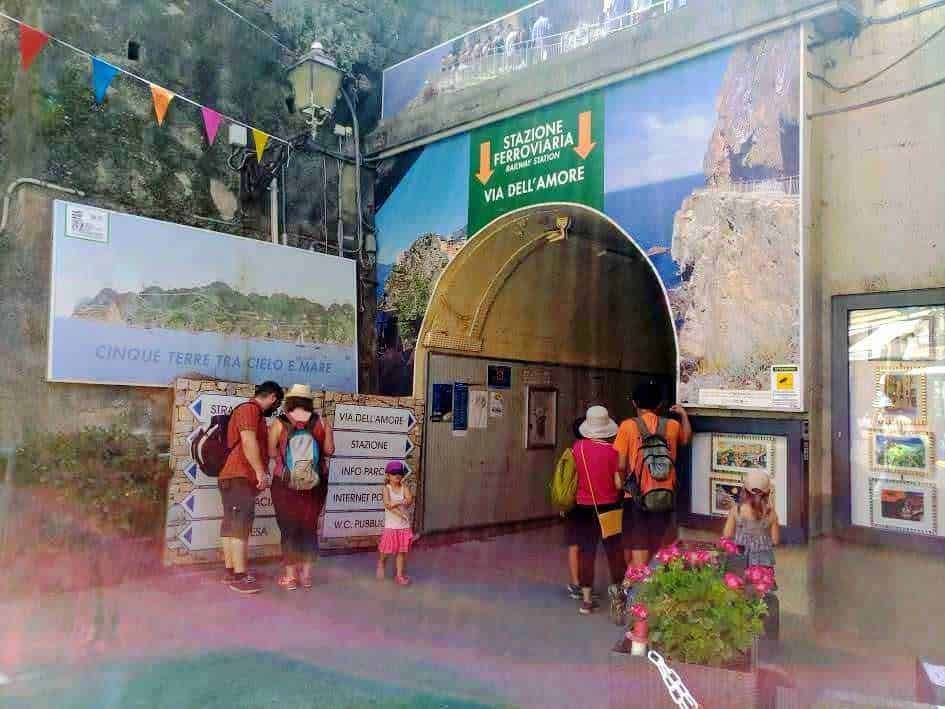 Stazione ferroviaria di Amalfi con ingresso e pannelli informativi, immagini di turisti e mamma con bambina, ambiente esterno colorato e accogliente, perfetto per scoprire la costa amalfitana.