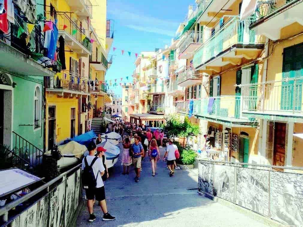 Colorata strada pedonale tra case colorate con balconi, panni stesi e decorazioni di bandiere, atmosfera vivace e turistica, giorno di sole in un quartiere pittoresco italiano.