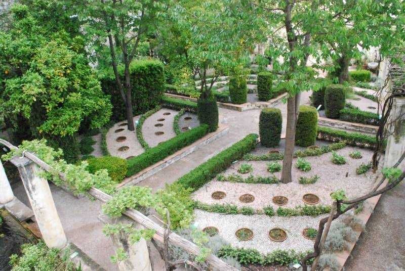 Bambini giocano nel giardino pubblico con panchine e aiuole verdi, atmosfera tranquilla e rilassante con piante e siepi ben curate, spazio all'aperto ideale per attività all'aria aperta e relax.