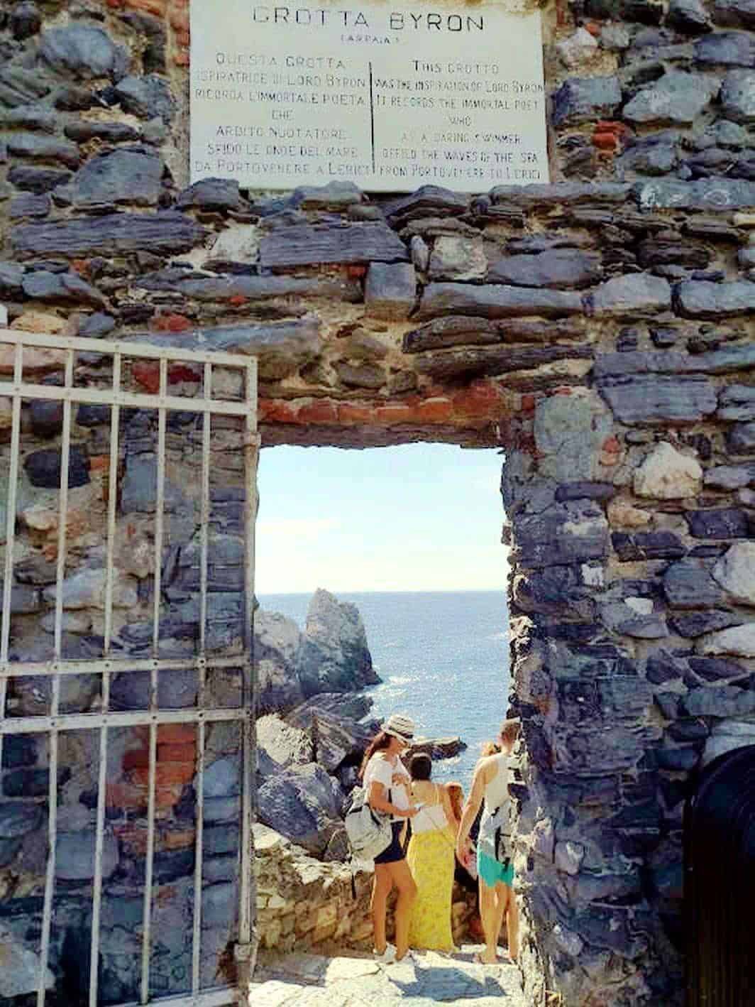 Antico ingresso di pietra al GROTTONE BYRON, vista sul mare, sulla costa e sullo strapiombo, con turisti che ammirano il paesaggio e l'atmosfera suggestiva di questa storica roccia nella Grotta Byron in Italia.