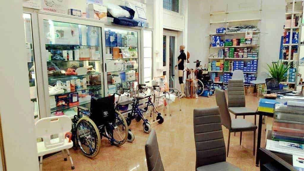 Sedie e deambulatori in farmacia, con scaffali pieni di prodotti medicinali e dispositivi medicali, ambiente accogliente e ben organizzato per assistere i clienti.