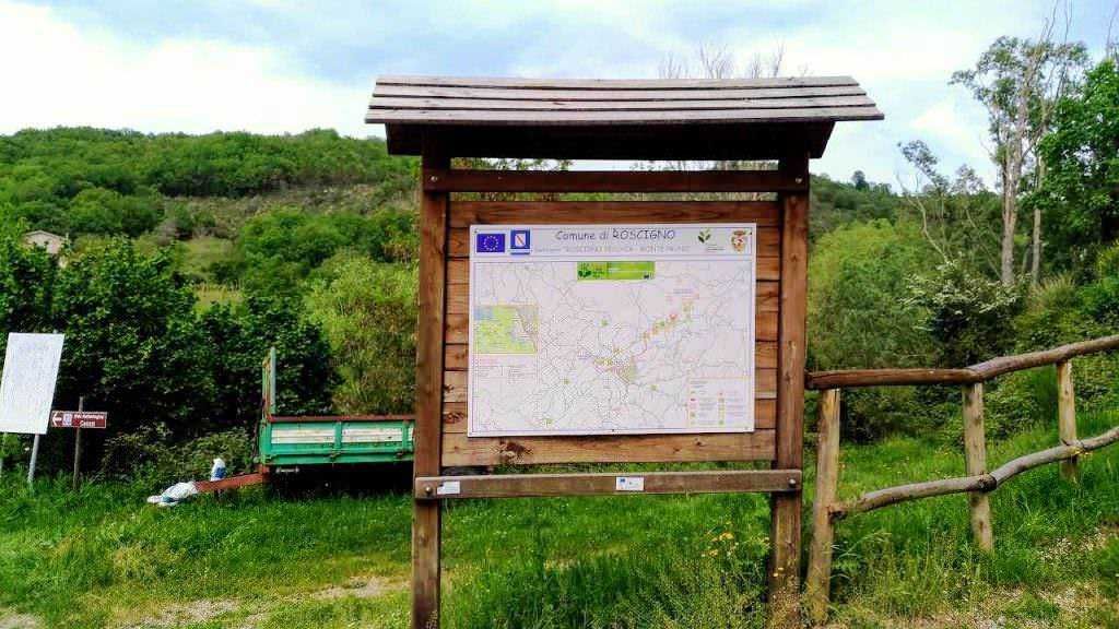 Cartello escursionistico in un'area naturale con mappa del sentiero e insegne informative, in una zona verde e protetta, perfetta per trekking e attività all'aperto in Toscana.