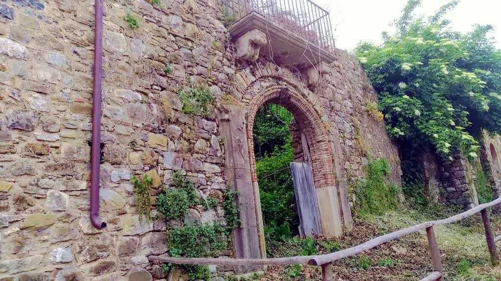 Antica porta in pietra con cascata d'acqua, immersa nel verde, resto di un edificio storico, ambientazione suggestiva e tranquilla.