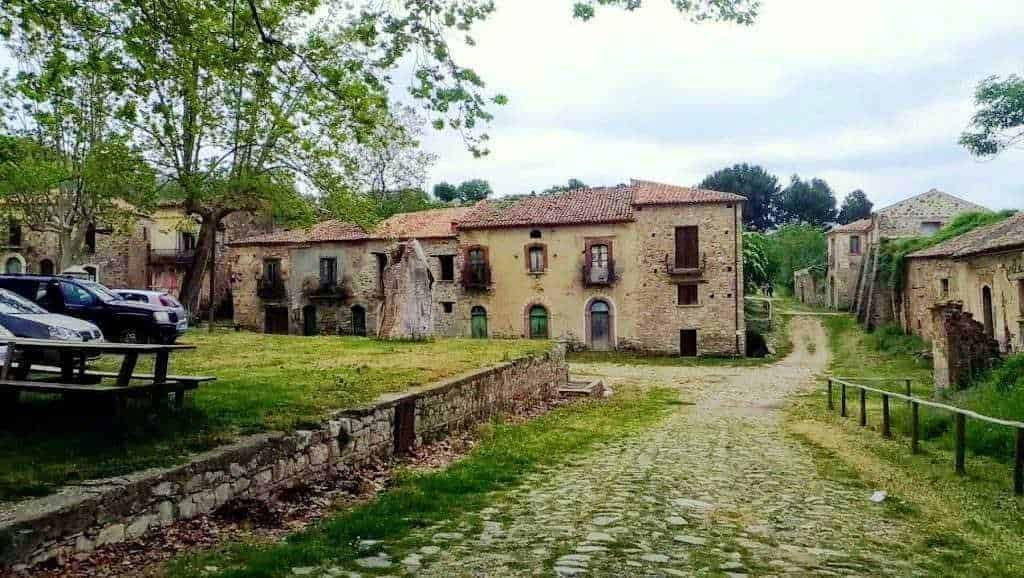 Vecchia casa di pietra immersa nella campagna italiana, con strade di ciottoli e vegetazione rigogliosa, perfetta per appunti sul blog dedicati a viaggi e storia locale.