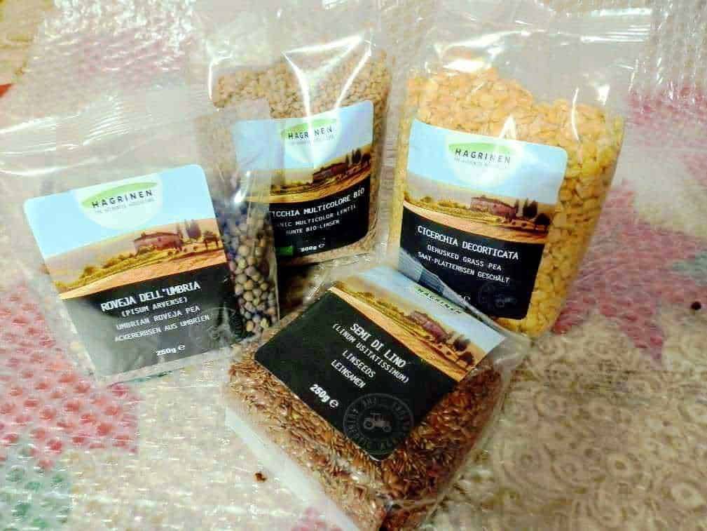 Fiocco di semi di cereali e legumi biologici assortiti, con confezioni di legumi secchi, sementi di piselli e altre varietà di legumi, ideali per coltivazione biologica e ricette salutari.