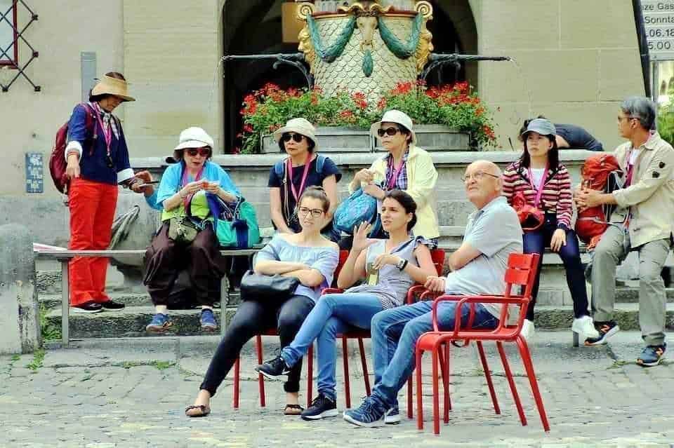 Diversi turisti seduti e in piedi davanti a un monumento storico, godendosi una visita guidata all'aperto in un'ambientazione urbana italiana.