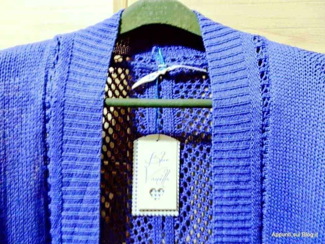 Veste blu con dettagli intrecciati e tessuto a rete, appesa su appendiabiti in stile vintage, con tag cucito a mano, ideale per look casual e alla moda.