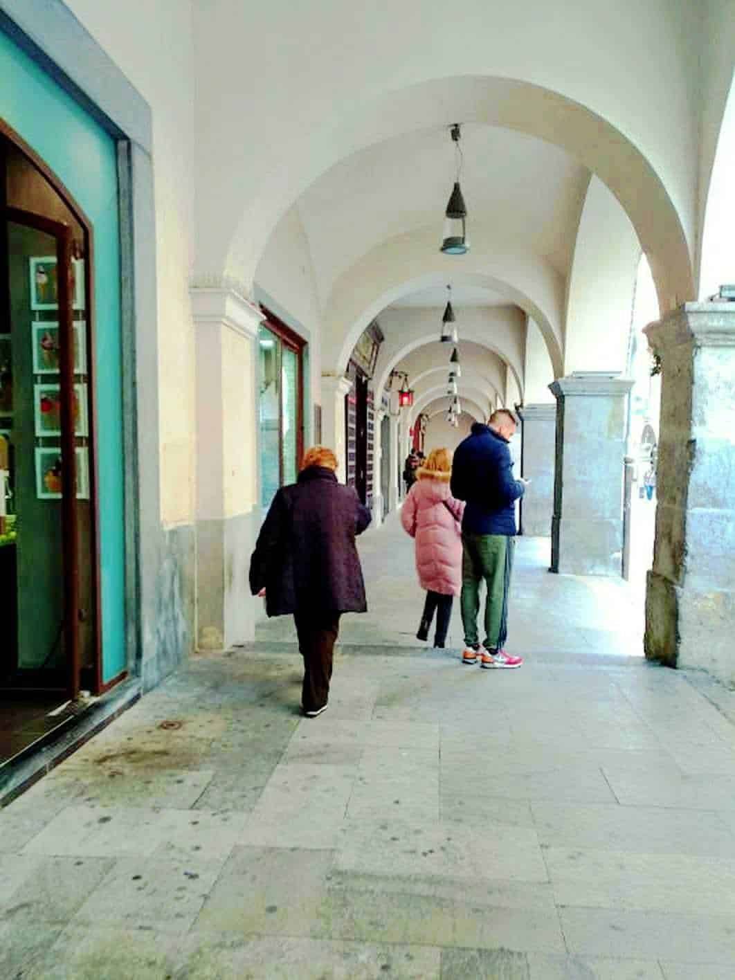 Passeggiata sotto i portici di una strada cittadina con persone che camminano, architettura storica, ambienti urbani, atmosfera autunnale.