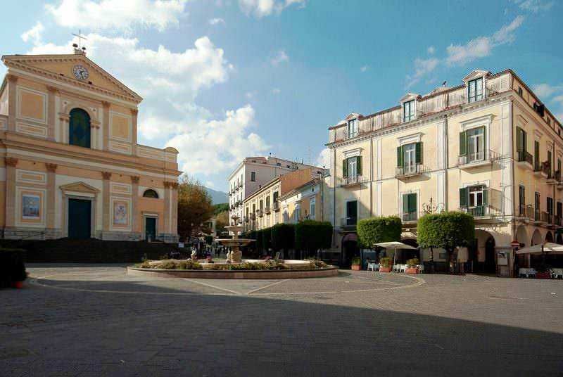 Fascia colonnata con chiesa storica e palazzi colorati in piazza centrale, atmosfera mediterranea, centro storico, edilizia storica, patrimonio culturale italiano, turismo, fotografia urbana.