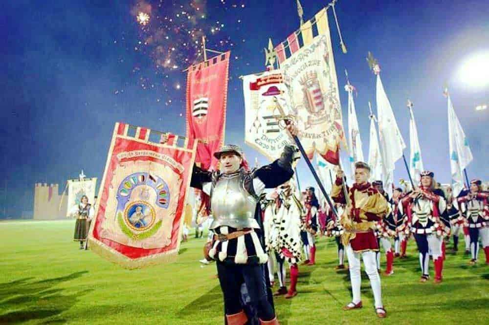 Bandiera storica del festival medievale con soldati in costume storico durante la manifestazione. Festeggiamento in stile medievale con falò e fuochi d'artificio in background, in una sera estiva.