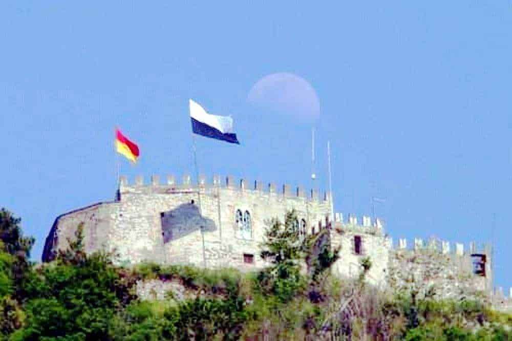 Castello antico con bandiere di Francia e Germania, situato su una collina, sotto un cielo azzurro, simbolo di storia e cultura europea, foto presa da Appunti Sul Blog.