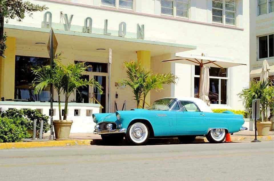 Vintage auto d'epoca Cadillac blu parcheggiata davanti a un hotel con piante e ombrelloni sulla veranda, atmosfera estiva e retrò.