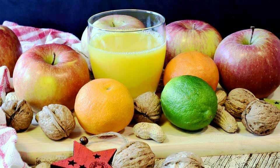 Mela, arancia, limone e noci fresche su un tagliere di legno con succo di frutta naturale in un bicchiere, ambientazione autentica e colorata.