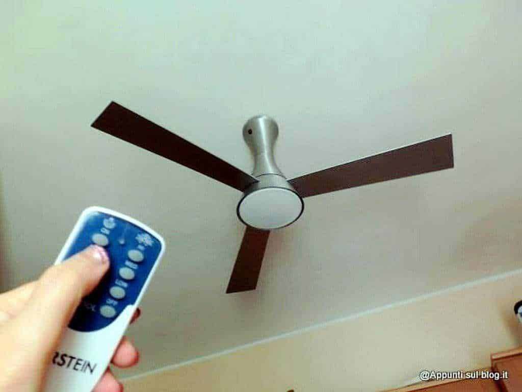 Ventilatore a soffitto con telecomando in mano, immagine di arredo casa, funzionamento facile, risparmio energetico, design moderno, ideale per ambienti domestici.
