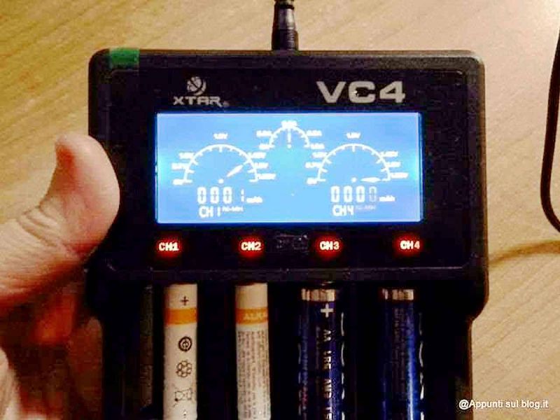 Caricabatteria pile Xtar VC4 con funzione Zero Volt 2 Caricabatteria pile con funzione zero volt: Relay screenshot of a multichannel digital voltmeter with a blue backlit display showing four analog signals. The device is held in a person's hand, with batteries visible at the bottom. The device is labeled "VC4" and has four channels, used for measuring electrical voltage.