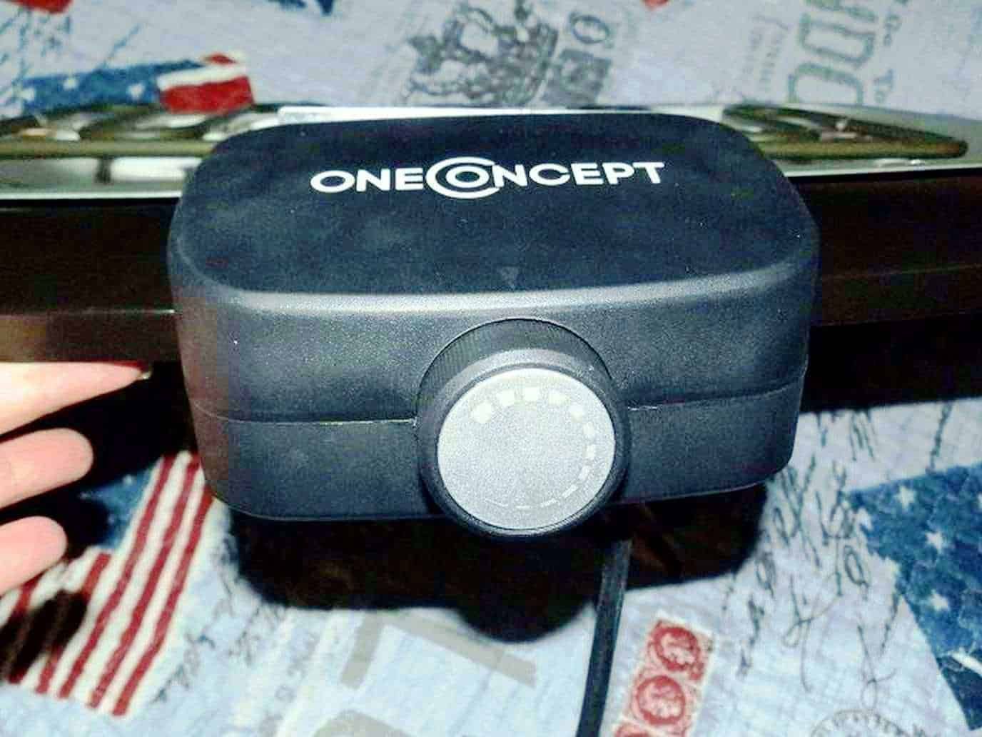 Alto testo: Vaporizzatore One Concept nero compatto, ideale per aromaterapia e terapie olistiche, posizionato su superficie decorata con motivi astratti e bandiere.