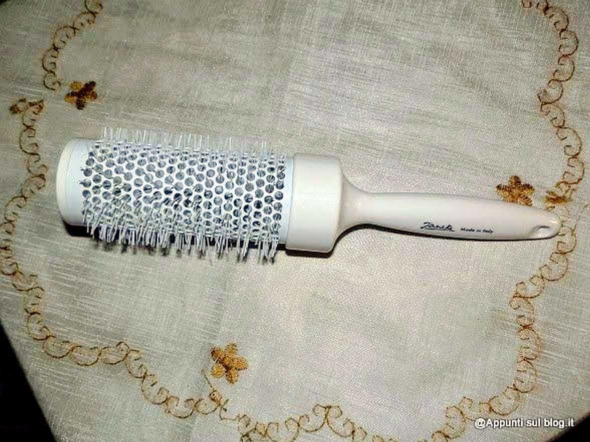Spazzola per capelli con manico bianco e setole in plastica, adatta alla cura dei capelli; oggetto per la cura personale, mostrato su tovaglia decorata.