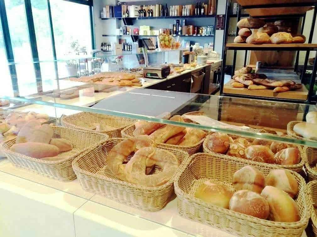 Pane fresco e prodotti da forno esposti in una panetteria moderna, con scaffali di ingredienti e attrezzature visibili sullo sfondo. Atmosfera accogliente e luminosa, ideale per una colazione o spuntino.