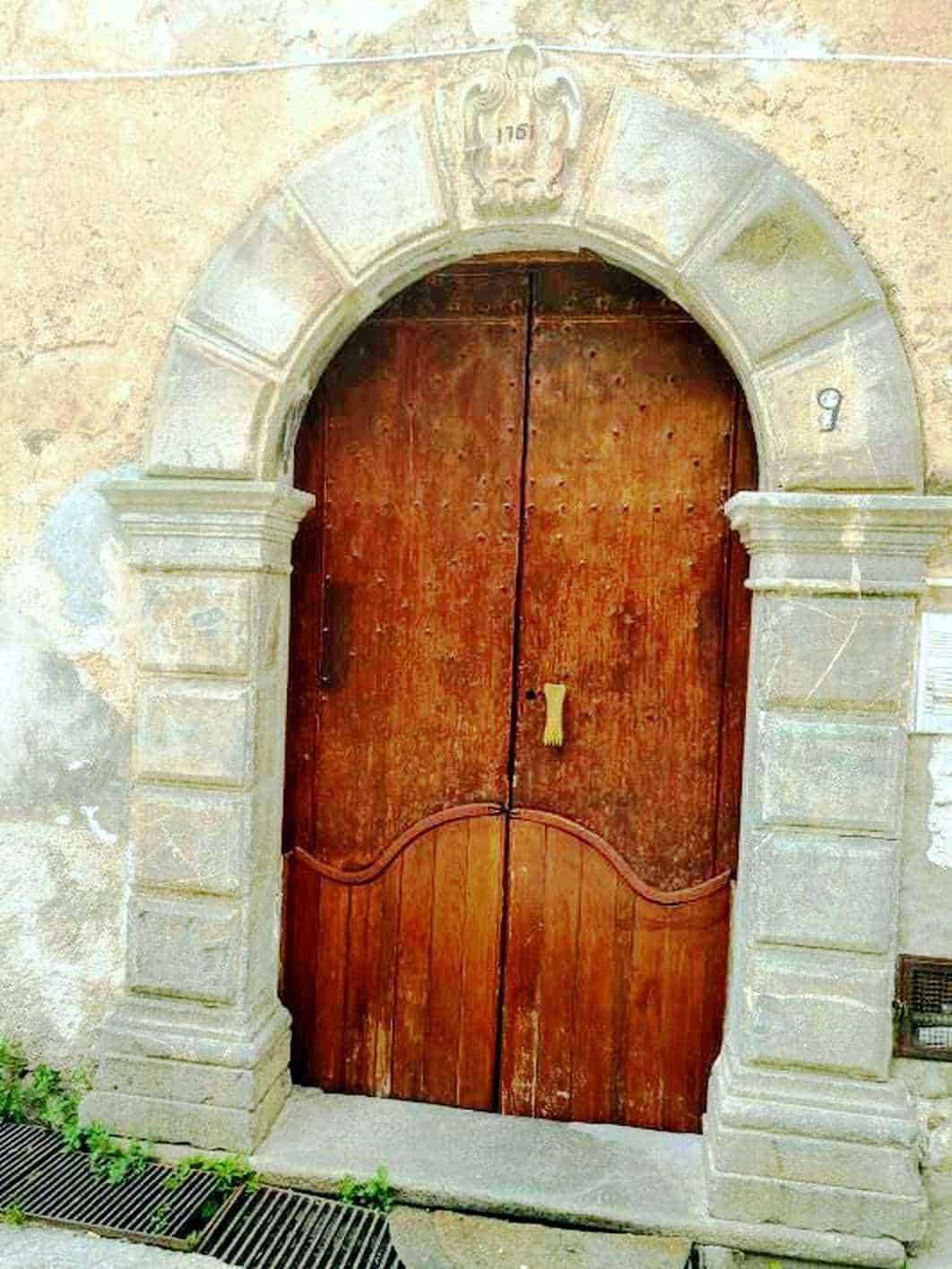 Porta in legno con arco in pietra, ingresso storico in stile italiano, dettaglio architettonico antico in pietra e legno, accesso a edificio storico, immagine di un'entrata tradizionale in Italia.