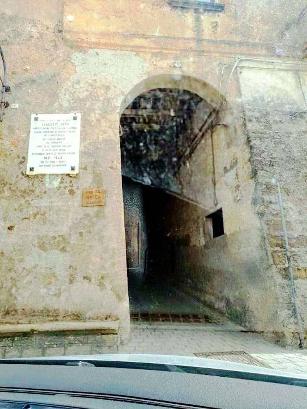 Vecchia porta in pietra con arco in stile storico, ingresso a un’antica via o cortile, dettagli di muri in pietra e sembra di un'area storica italiana.