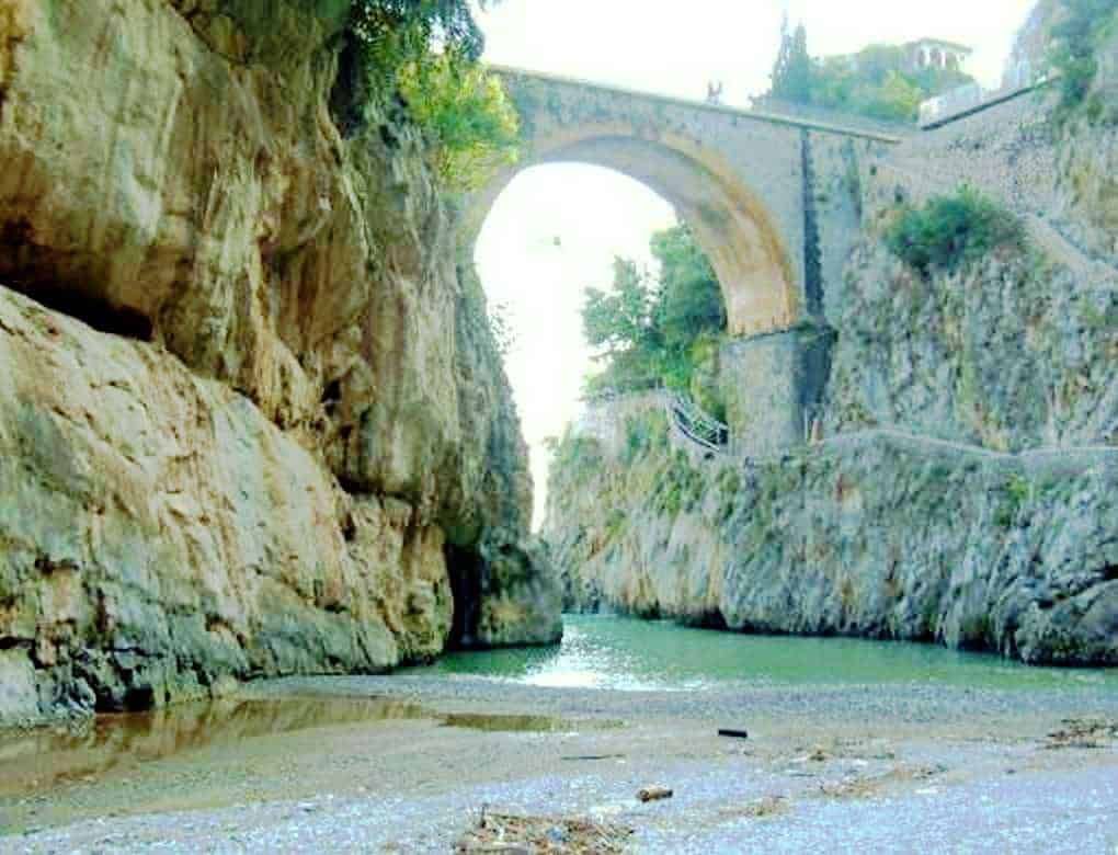 Ponte storico in pietra sopra un fiume con scogliera rocciosa, paesaggio naturale e architettura antica in zona panoramica.