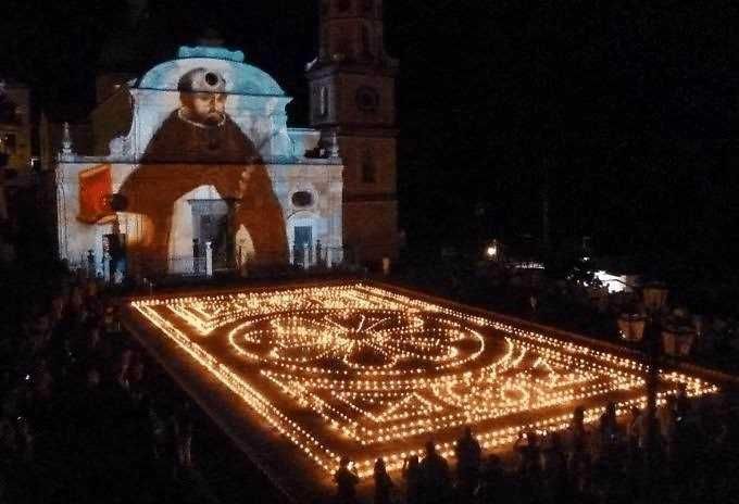 Splendida rappresentazione con luci e fuochi d'artificio sulla piazza di notte, con una chiesa storica sullo sfondo, che crea un'atmosfera magica e suggestiva, ideale per eventi e festività.
