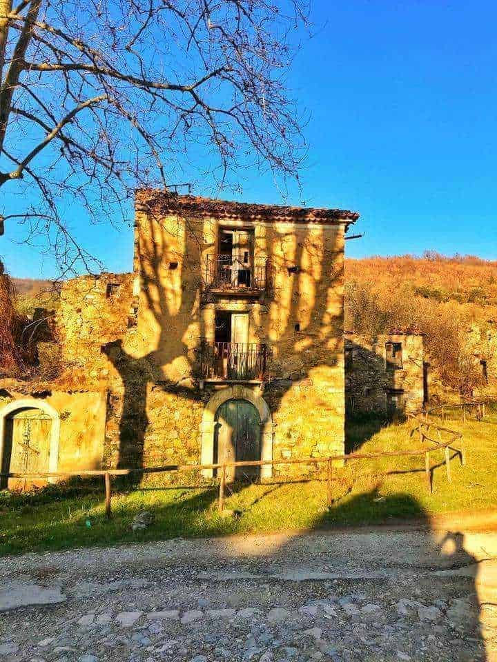 Vecchia chiesa in rovina di epoca storica, con muri in mattoni rossi e dettagli architettonici decadenti, circondata da alberi verdi e un cortile erboso sotto un cielo nuvoloso, suggestiva e affascinante.
