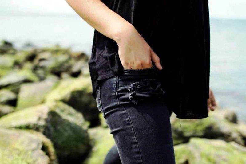 Dean Juster, jeans d'alta moda made in Italy 3 Vestito casual donna con jeans strappati e giacca nera, stile streetwear, ambientazione all'aperto sulla spiaggia.