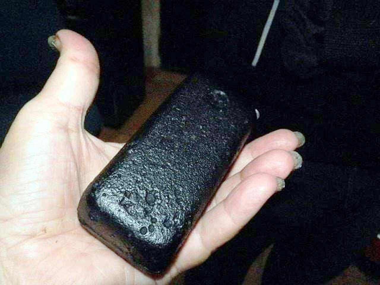 Briko di carbone minerale nero e compatto, mani che lo tengono, sfondo scuro e non dettagliato.