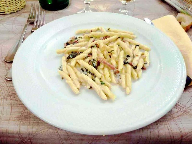 Pasta fatta in casa con crema di formaggio, prosciutto e verdure, piatto tipico della cucina italiana, servito in un ristorante vicino al mare, perfetto per una cena gourmet.