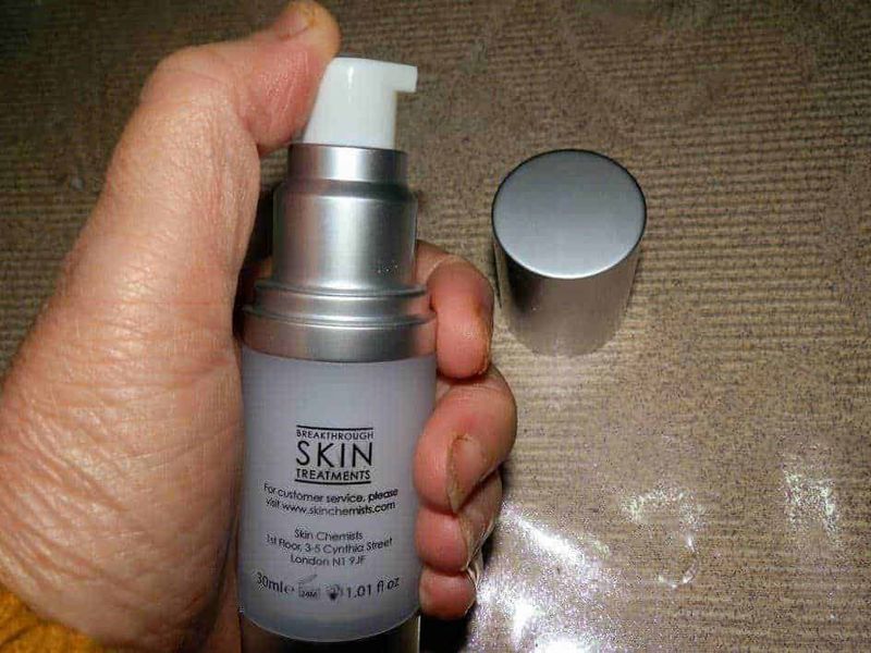 skin Chemists: cosmetici per rinnovare e proteggere la pelle 3 Flacone di trattamento per la pelle con etichetta "Skin Treatments" e tappo argento, di fronte a superfice in legno con polvere bianca.
