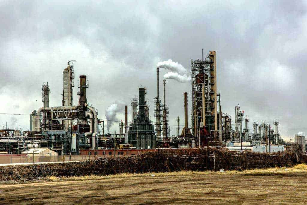 Impianto industriale petrolifero con torri di raffinazione e emissioni di gas industriali inquinanti.