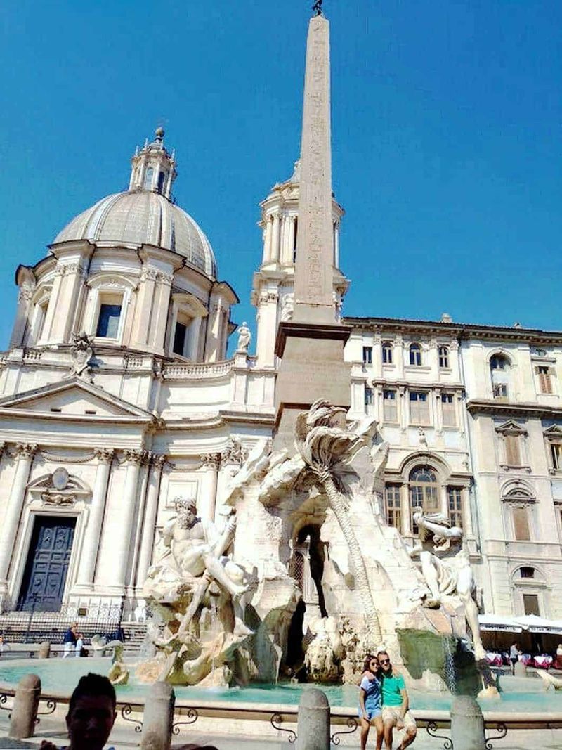 Virail: visita Roma e Verona in 1 giorno 6 Fountain of the Four Rivers in Piazza Navona, Rome, Italy, featuring majestic baroque sculptures and the ancient Egyptian Obelisk of Domitian, set against the backdrop of the Church of Sant'Agnese in Agone.