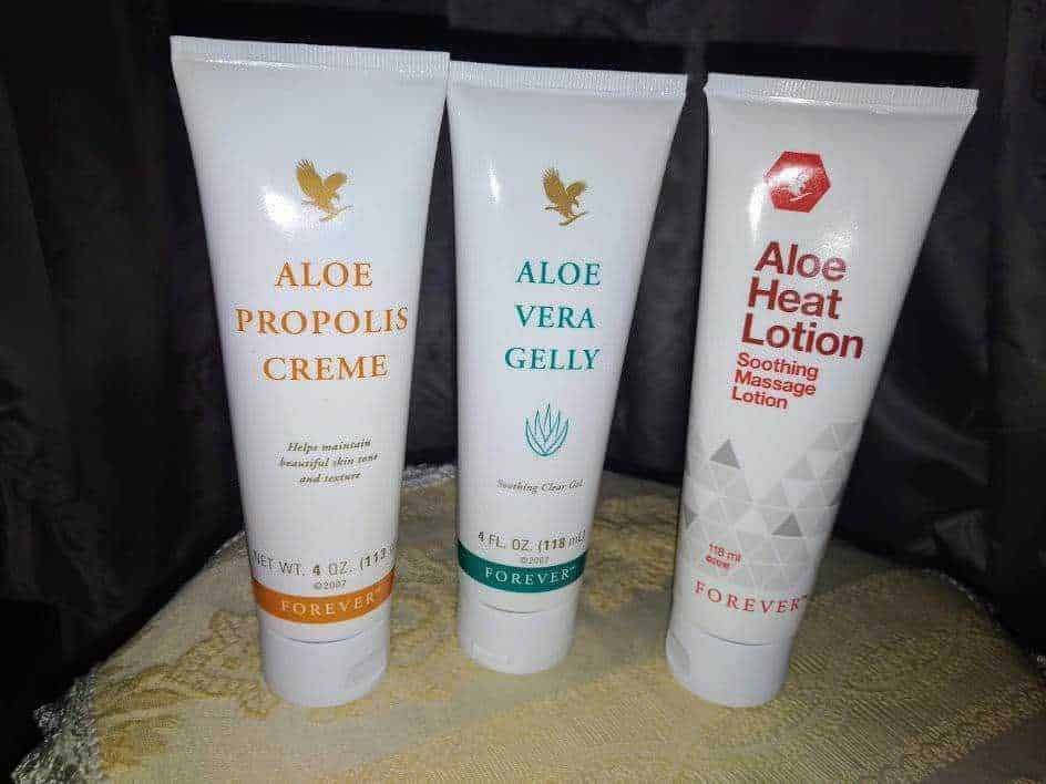 Aloe propolis crema, aloe vera gelly e aloe heat lotion in tubo, prodotti per il benessere della pelle, cura naturale, idratazione e massaggi, rivestiti di confezioni bianche con dettagli colorati, presentati su tovagliolo di stoffa.