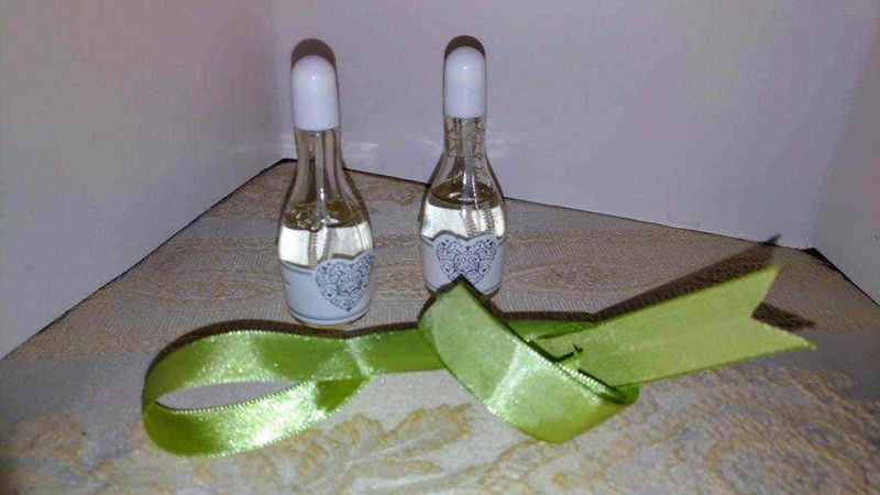 My Bomboniere: idee e novità per eventi importanti 4 Piccole fiale di profumo con cuore decorato, lunghezza media, in vetro trasparente, sul tavolo di legno con nastro verde brillante e sfondo neutro.