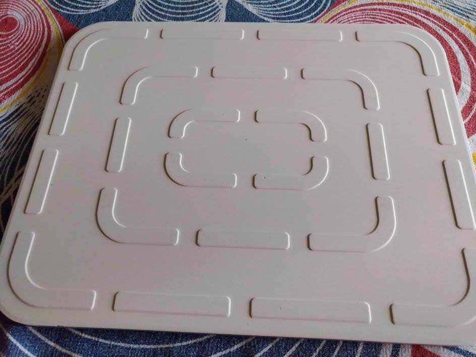Piatto in plastica bianca con motivo geometrico, ideato per contenere alimenti o snack; superficie liscia con dettagli incavati.