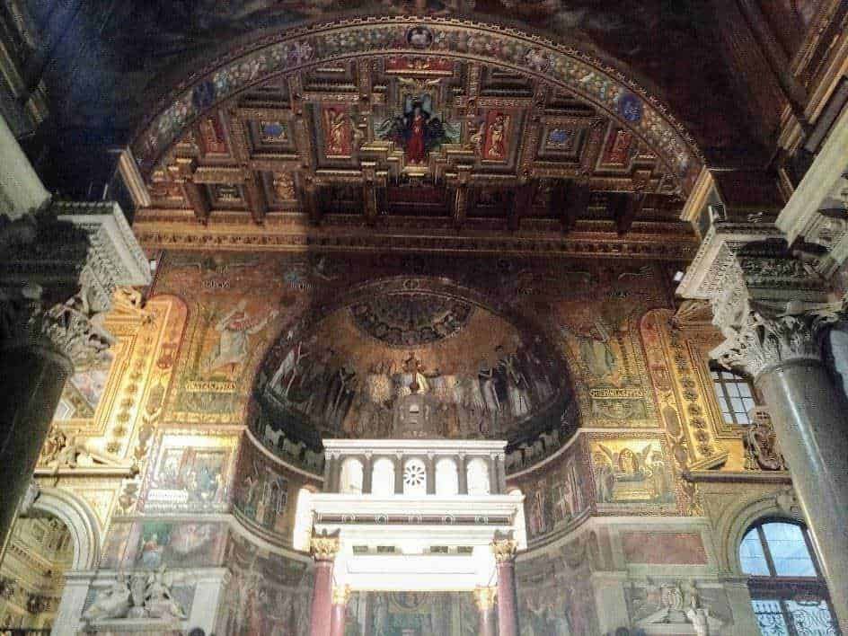 Finestre di una chiesa barocca decorata con affreschi e dettagli dorati che rappresentano scene religiose, con colonne in marmo e archi scolpiti, creando un ambiente sacro e storico.