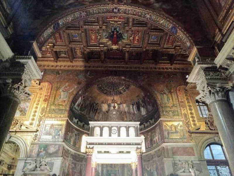 Roma capitale tour in mesi caldi 11 Finestre di una chiesa barocca decorata con affreschi e dettagli dorati che rappresentano scene religiose, con colonne in marmo e archi scolpiti, creando un ambiente sacro e storico.