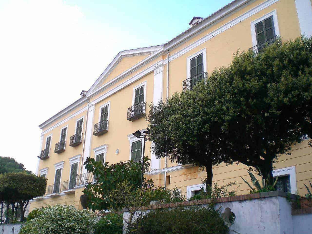 Villetta storica in stile italiano con balconi e finestre a vetri, circondata da alberi e piante verdi, in un quartiere tranquillo e ricco di fascino.
