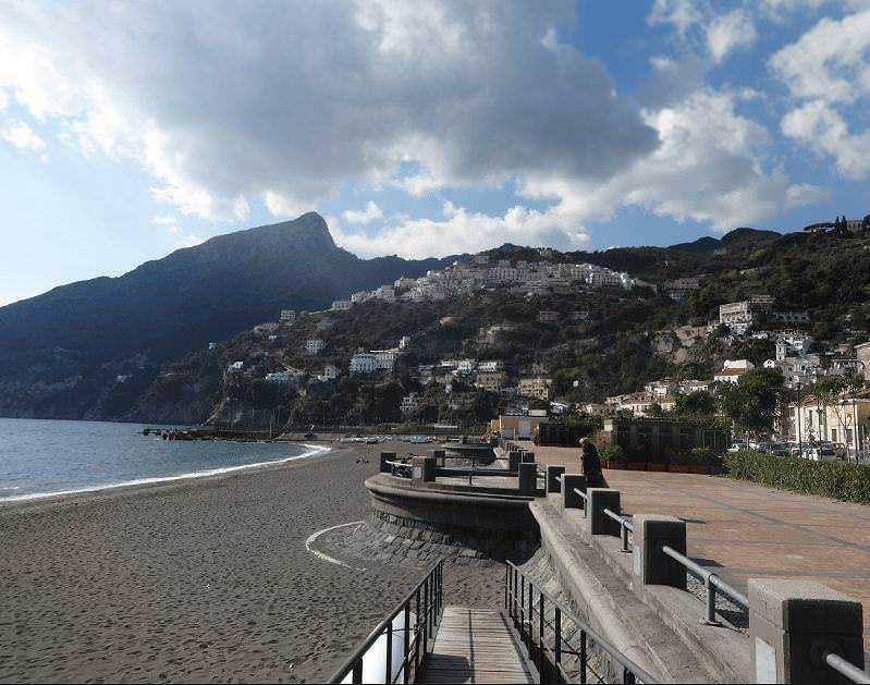Spiaggia di Positano, costa amalfitana, con case colorate su scogliera, promontorio suggestivo e mare tranquillo, perfetta meta per vacanze estive e relax in Italia.