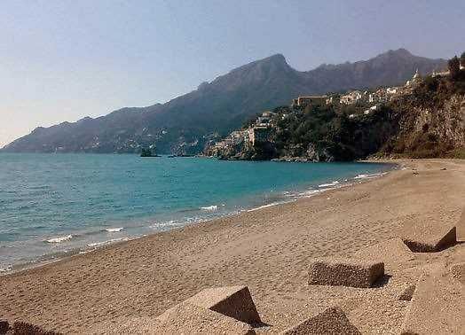 Spiaggia tranquilla con sabbia dorata e mare azzurro, fronte Monti Lattari e Costa Amalfitana, perfetta per relax e vacanze estive in Campania.