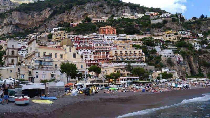 Casecolorate e affascinanti sulla scogliera di Positano, costiera amalfitana, Italia, con spiaggia affollata, ombrelloni e turisti in estate, atmosfera vivace e panorami mozzafiato.