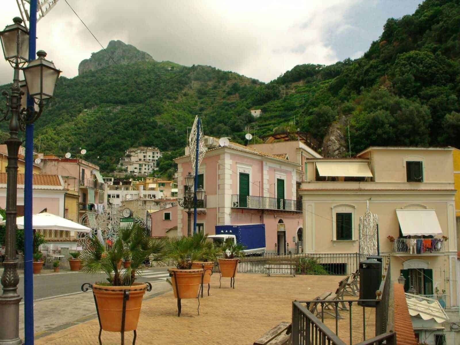 Cetara, paesino sul mare con case colorate e terrazze, situato tra montagne verdi, con panchine e piante in vaso in primo piano, atmosfera tranquilla e suggestiva.