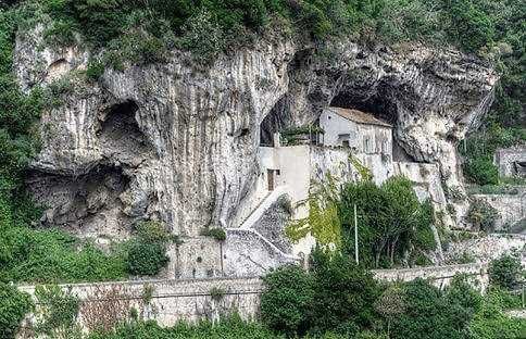 abbazia di Santa Maria de Olearia costruita nelle rocce di un paesaggio montano con vegetazione lussureggiante e strade serpeggianti nelle vicinanze, esempio di architettura integrata nella natura.