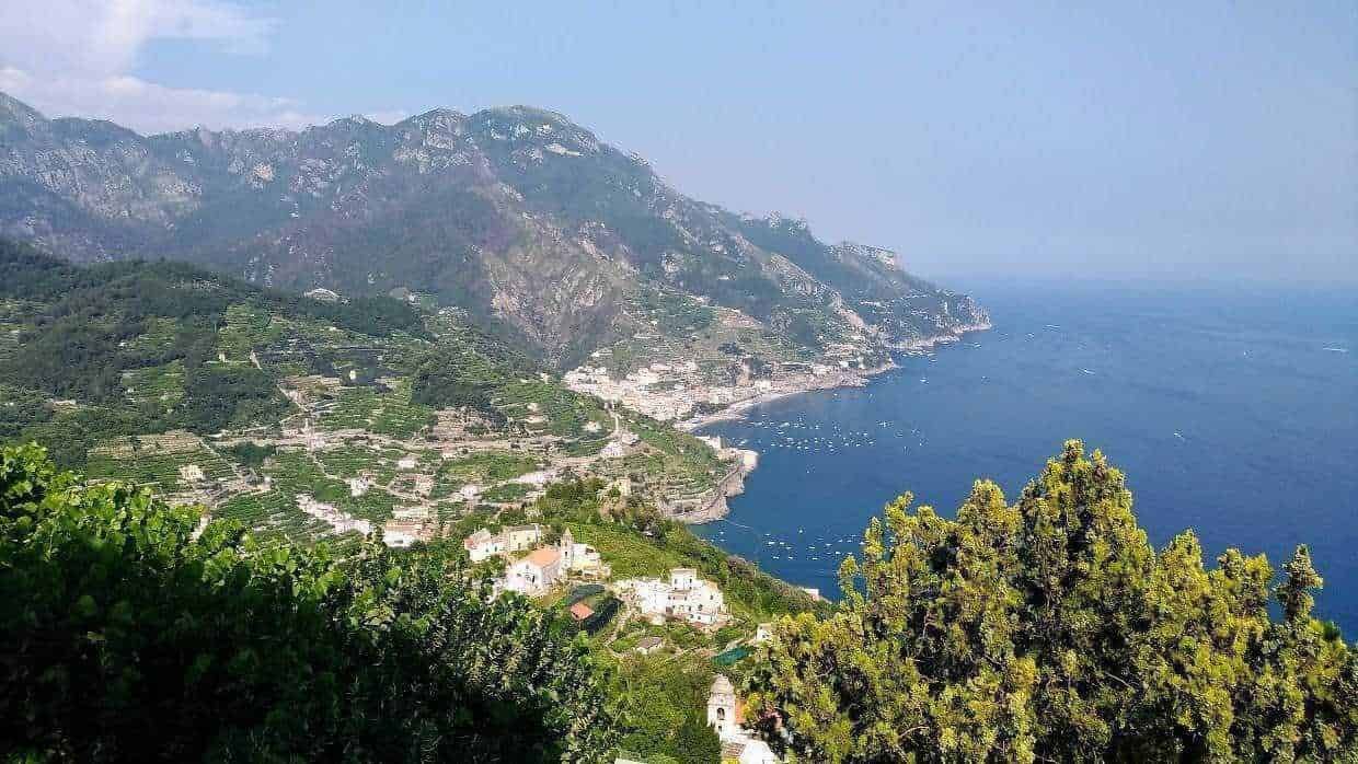 Vista panoramica della Costiera Amalfitana con colline verdeggianti, case bianche e il mare cristallino, ideale per vacanze in Italia.