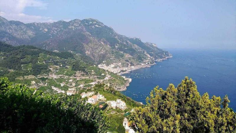 Costiera amalfitana, 18 borghi da visitare in 40 km 3 Vista panoramica della Costiera Amalfitana con colline verdeggianti, case bianche e il mare cristallino, ideale per vacanze in Italia.