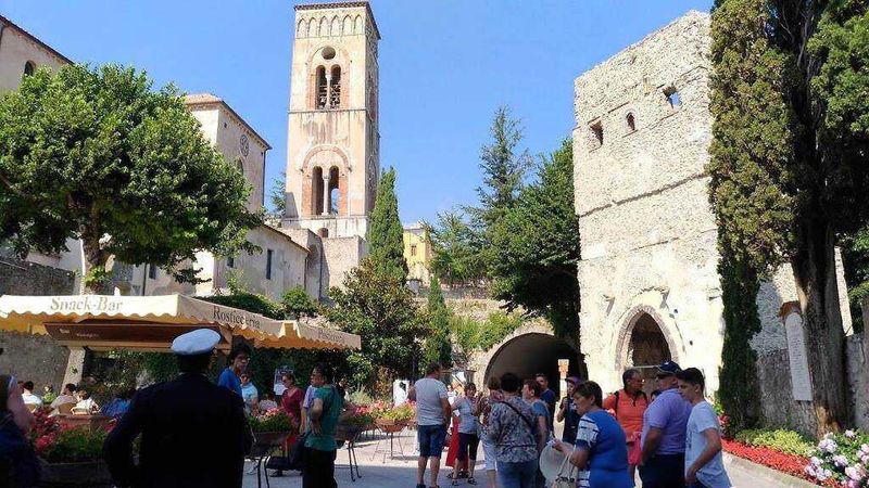 RAVELLO, Finestra nel cuore di un antico borgo italiano con torre medievale, gruppi di turisti e chiosco snack-bar, atmosfera tipica, architettura storica, turismo culturale e paesaggio urbano, Italia.