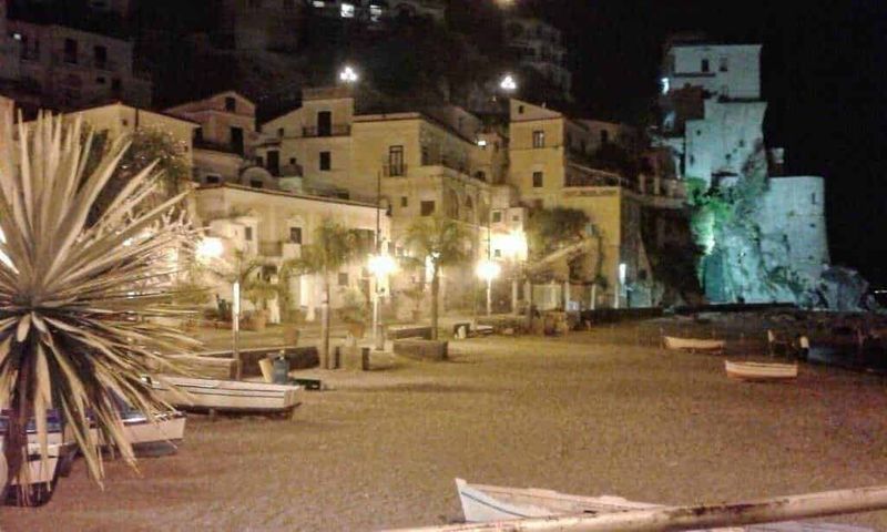 Luminosa veduta di Cetara, un caratteristico villaggio sul pendio di una collina con case bianche e strette strade, circondato da verde natura e montagne, scenario perfetto per scoprire le meraviglie della Costiera Amalfitana.