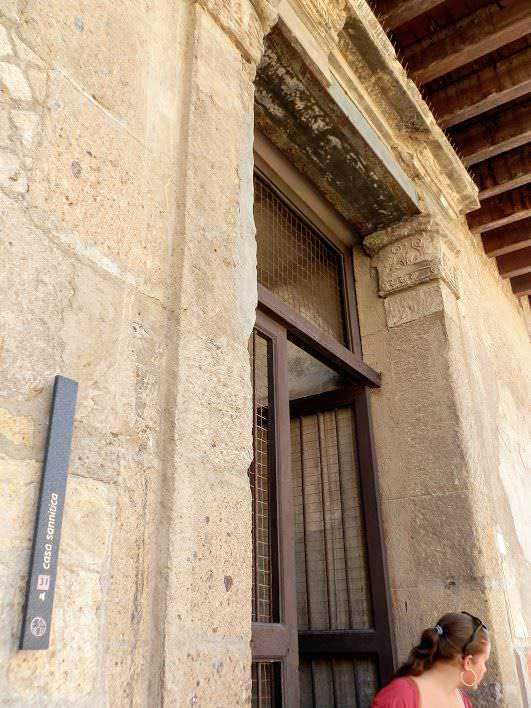 Coperchio in vetro a protezione della porta d'ingresso di un edificio storico, dettagli architettonici in pietra, ambiente urbano, donna con capelli ricci e occhiali da sole.