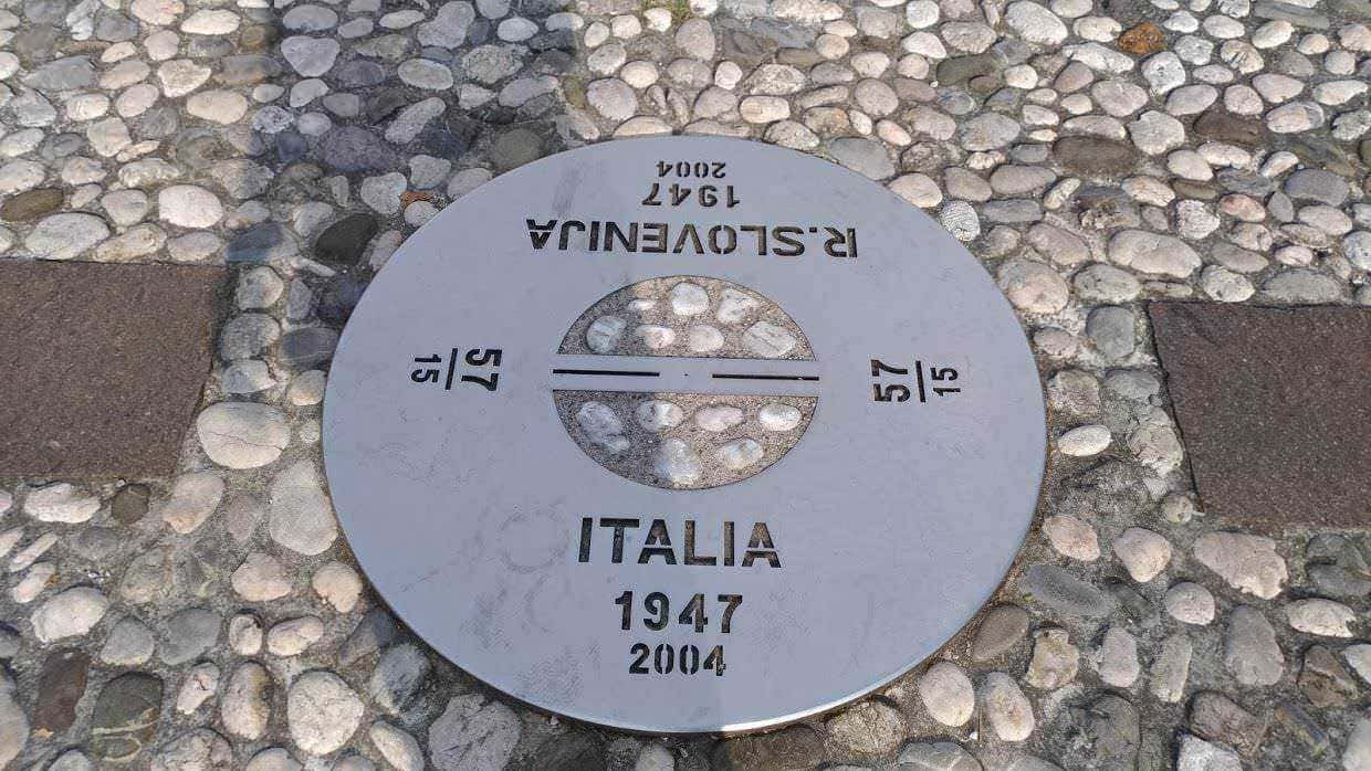 Piastra commemorativa Italia 1947-2004, simbolo di unità e memoria storica, situata su lastra di pietra mista a ciottoli, rappresenta un punto di riferimento culturale e storico in Italia.